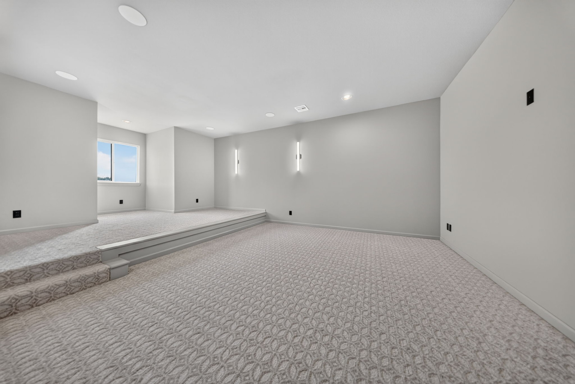Carpeted tiered media room with linear wall sconces in a Broken Arrow Oklahoma luxury new build