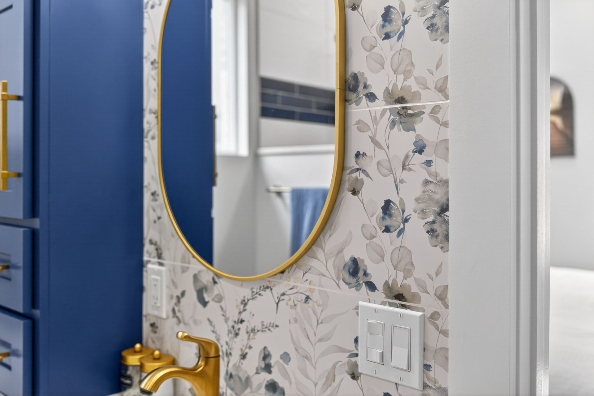 Blue vanity, floral wallpaper and gold oval mirror detail photographed by Killer Visuals