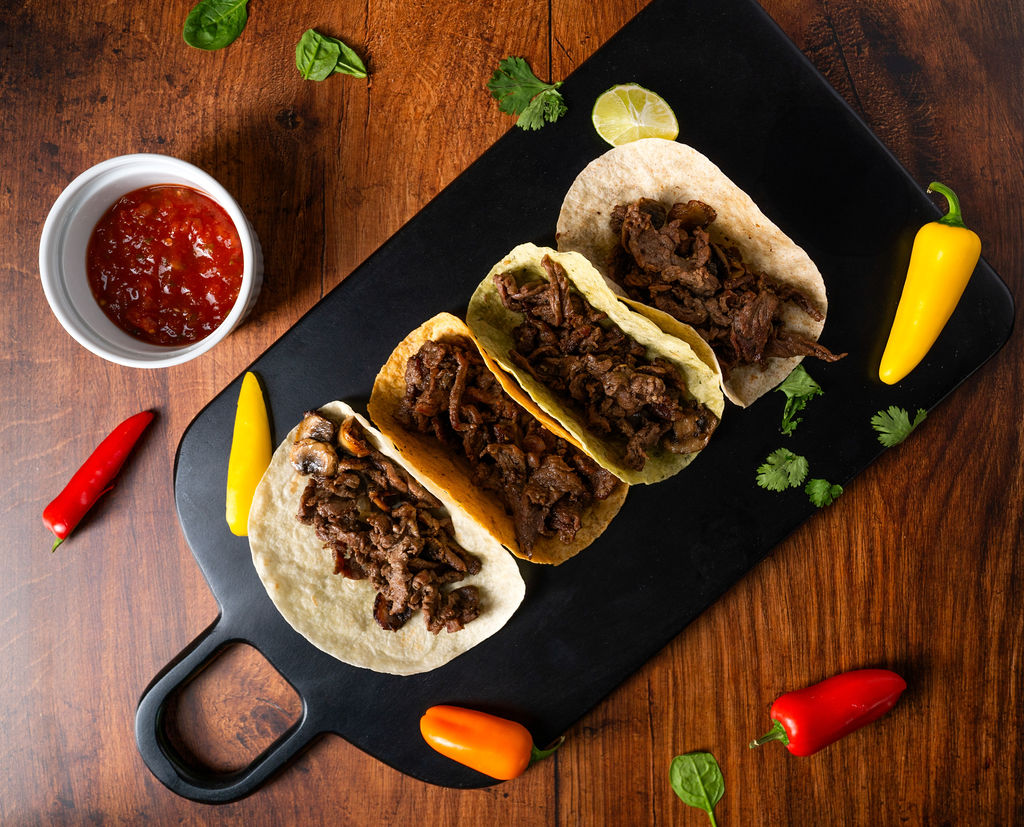 Three steak street tacos plated on a black board with salsa and peppers